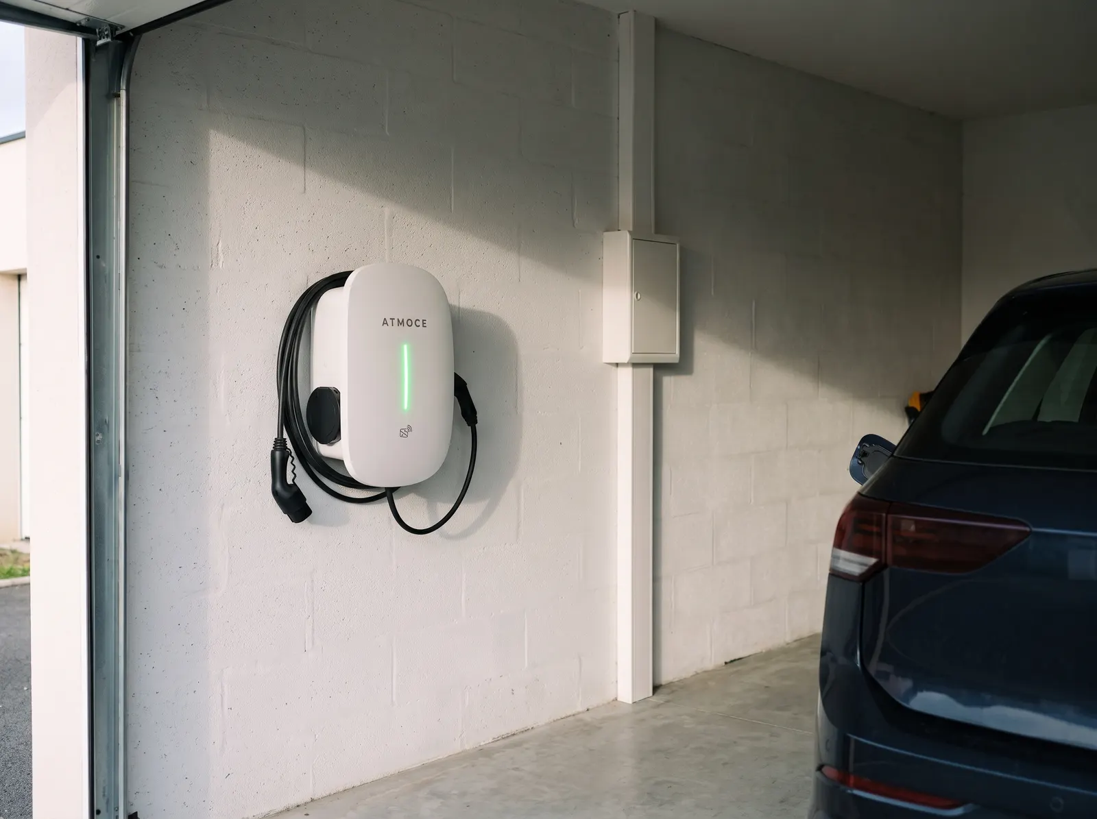 Borne de recharge ATMOCE installée dans un garage à côté d'un véhicule électrique